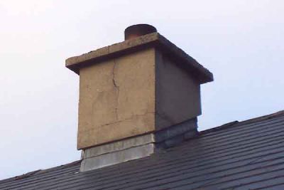 A chimney stack with cracked render above a roof