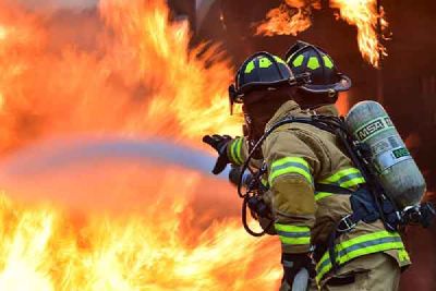 Two firefighters in breathing apparatus spray water on a fire