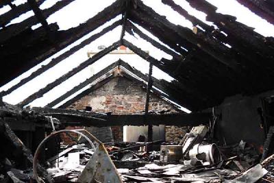 The burnt roof timbers of a house, open to the sky, with debris on the floor below