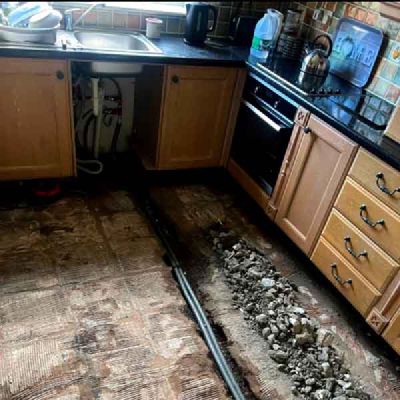 A kitchen with the floor lifted and a pipe laid in a trench beside the units