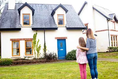 A woman and a child stand on the grass and look at a house with a blue front door